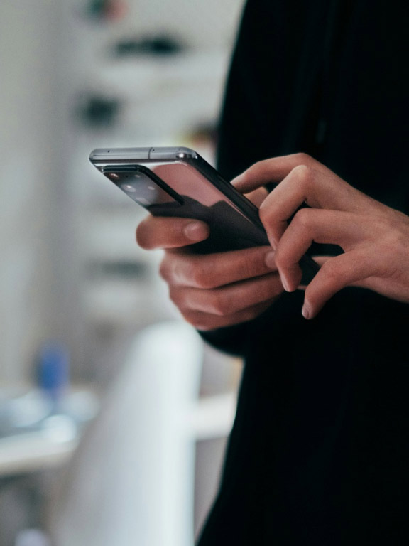 Eine Person hält ein Smartphone in den Händen und tippt auf dem Bildschirm. Der Hintergrund ist unscharf, die Szene wirkt alltäglich und modern.